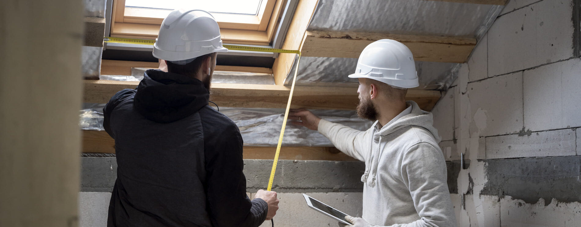 2 hommes sous les combles d'une maison, en train de prendre des mesures pour effectuer des travaux.