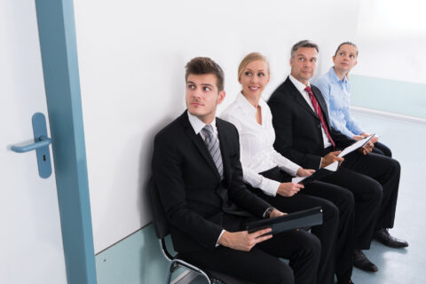 Hommes et femmes assis, attendant un recruteur dans une salle aux murs blancs