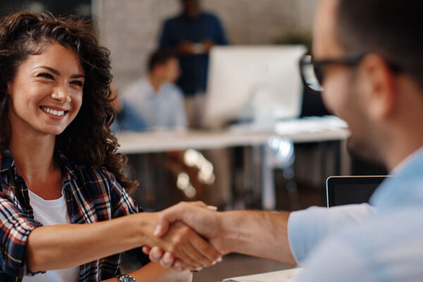 jeune femme brune avec les cheveux longs frisés qui serre la main d'un homme à chemise bleue
