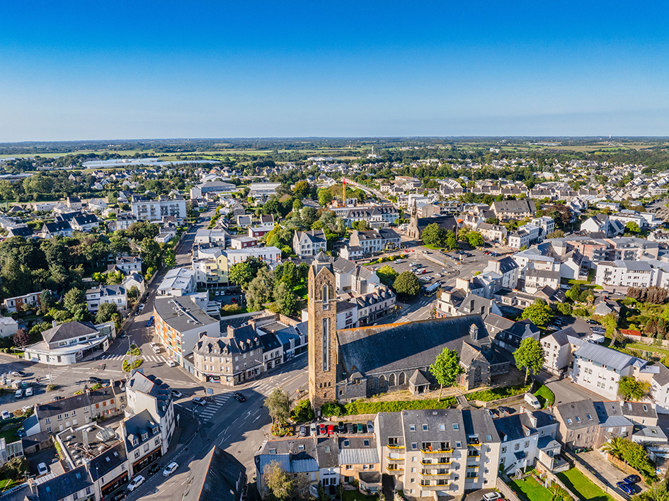 Une vue aérienne de la Ville de Guipavas avec son église au centre et un bel aperçu du centre-ville sous un grand ciel bleu.