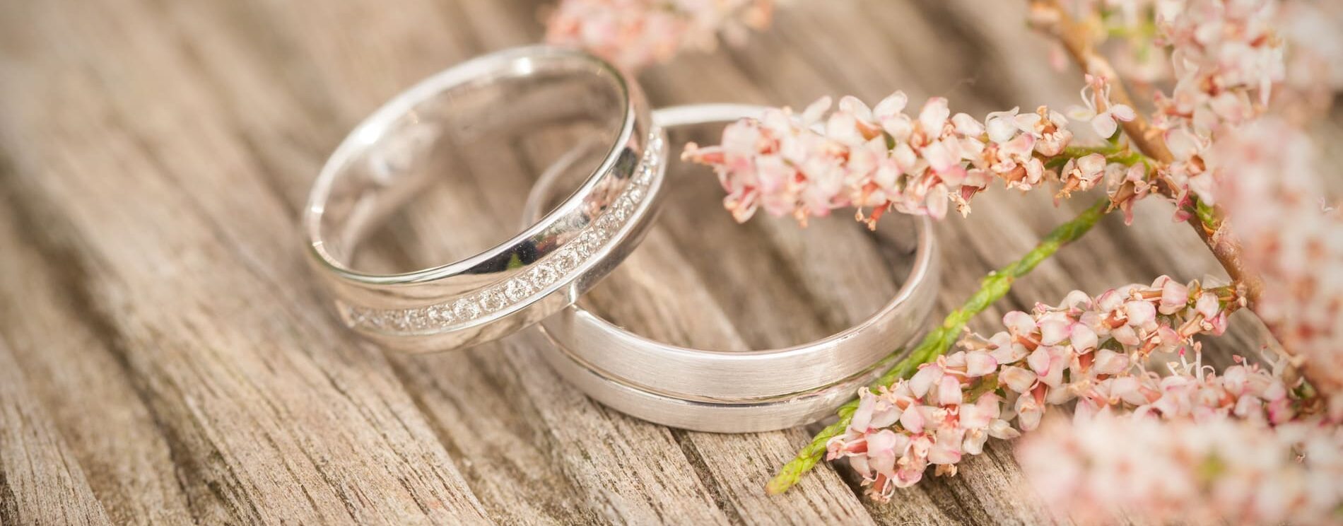 gros plan sur 2 alliances posée sur une table en bois. Fleurs rose en décoration