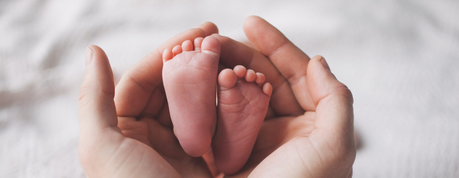Gros plan sur 2 mains qui tiennent entre elles les pieds d'un bébé