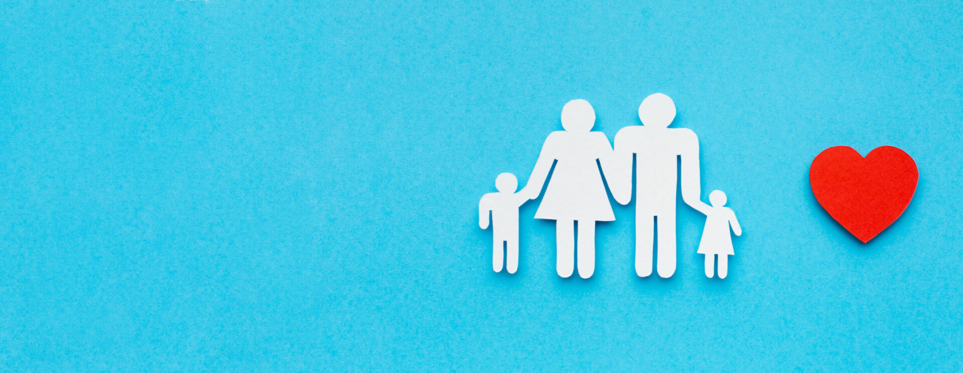 4 personnage en papier représentant une famille, posés sur un fond bleu. Un coeur rouge est placé à droite de la famille.