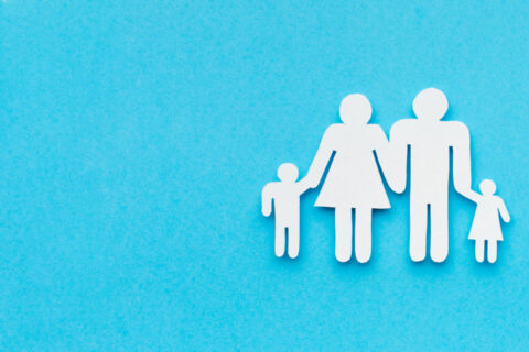 4 personnage en papier représentant une famille, posés sur un fond bleu. Un coeur rouge est placé à droite de la famille.