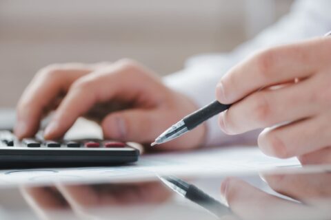 gros plan sur des maions tenant un stylo et appuyant sur les touches d'une calculatrice