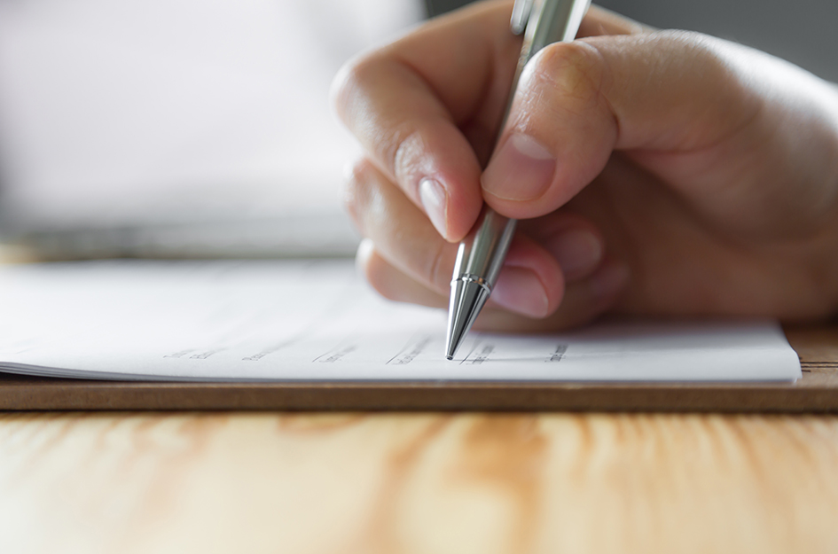 Une main tenant un stylo pour écrire sur une feuille de papier