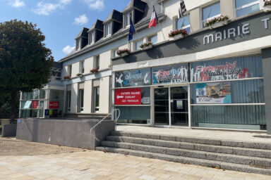 façade de la mairie de guipavas. Bâtiment de type années 1970-1980 avec une grande baie vitrée en façade. L''entrée est surplombée de 3 drapeaux : le drapeau français, le drapeau européen et le drapeau breton.