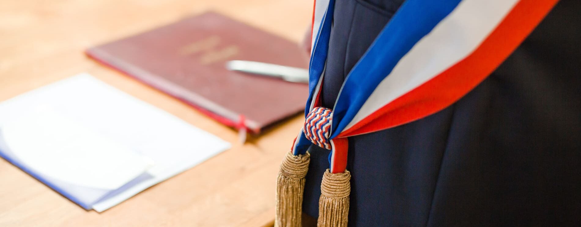 Homme en costume bleu marine. Un focus est fait sur l'écharpe bleu blanc rouge qu'il porte.
