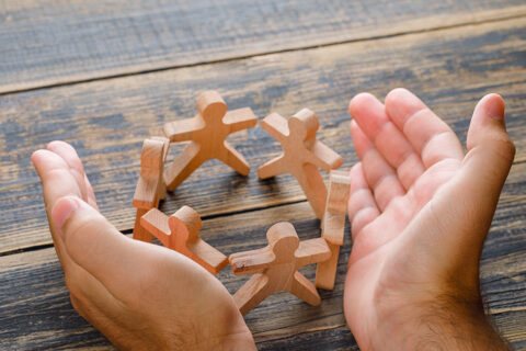 deux mains d'homme ouvertes sur de petites figurines en bois qui représentent des personnes.