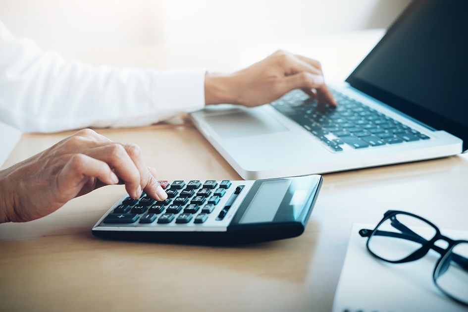 Homme en chemise blanche qui pose une main sur une calculatrice et l'autre sur un clavier d'ordinateur portable.