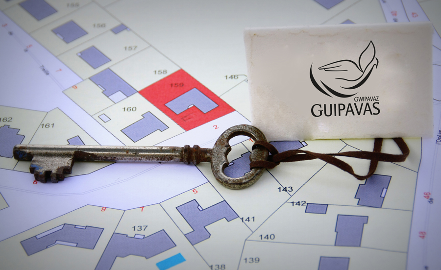 Clé ancienne à laquelle est attachée une étiquette avec le logo de la ville de Guipavas. En arrière-plan, un plan cadastral sur fond blanc.